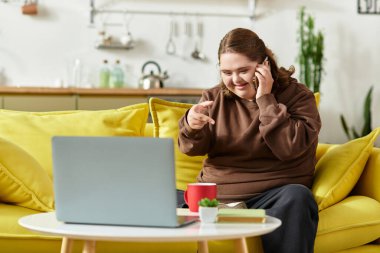 Down sendromlu neşeli genç bir kadın rahat bir koltukta oturup telefonla konuşuyor ve gülümsüyor..
