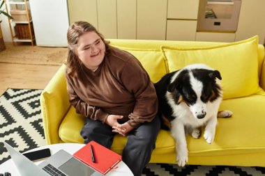 Genç bir kadın, köpeğiyle oturma odasındaki parlak sarı kanepede vakit geçirmekten hoşlanıyor..