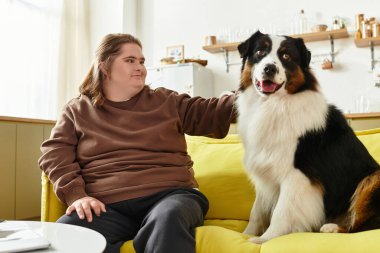 Down sendromlu genç bir kadın evinde gevşiyor. Dost canlısı köpeğini koltukta okşuyor..