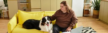 Down sendromlu genç bir kadın parlak sarı bir kanepede oturuyor, rahat bir evde köpeğini okşuyor..