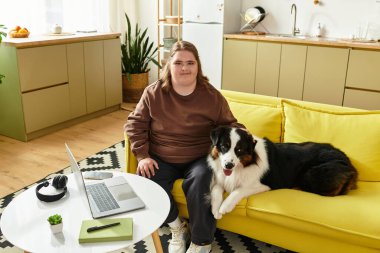 Down sendromlu genç bir kadın sarı bir kanepede köpeğiyle birlikte parlak bir odada oturuyor..