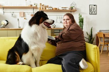 Genç bir kadın parlak bir kanepede oturuyor ve köpeğiyle oturma odasında mutlu bir şekilde vakit geçiriyor..