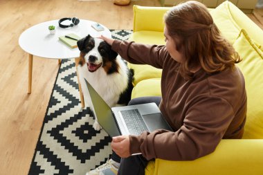 Down sendromlu genç bir kadın evinde rahat bir kanepede otururken köpeğini severek besliyor..