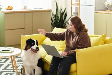 Down sendromlu genç bir kadın rahat sarı bir kanepede köpeğiyle seve seve etkileşime girer..