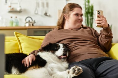 Mutlu genç bir kadın, sarı bir kanepede köpeğiyle birlikte huzurlu bir anın tadını çıkarıyor..