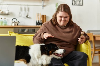 Down sendromlu genç bir kadın köpeğiyle oynarken kanepede dinleniyor..