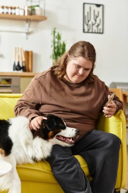 Genç bir kadın oturma odasında parlak sarı bir kanepede otururken köpeğiyle vakit geçirmekten zevk alıyor..