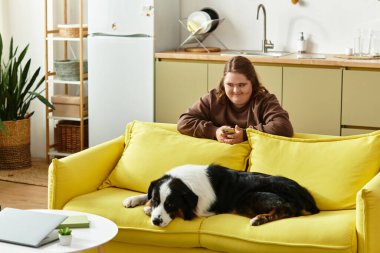 Genç bir kadın köpeğiyle birlikte evinde güneşli bir koltukta otururken telefonuna odaklanıyor..