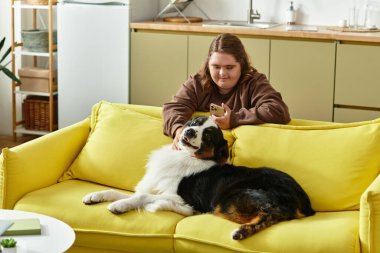 Güneşli bir günde evinde köpeğinin yanında oturan genç bir kadın telefonunu kullanarak gülümsüyor..