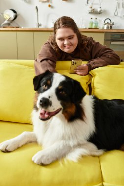 Neşeli genç bir kadın evdeki parlak sarı bir kanepede dinlenirken köpeğiyle etkileşime girer..