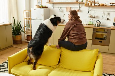 Genç bir kadın parlak sarı bir kanepede oturuyor, sıcak ve davetkar bir evde köpeğiyle meşgul..
