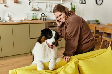 Down sendromlu genç bir kadın telefonda konuşurken gülümsüyor ve köpeğiyle vakit geçiriyor..