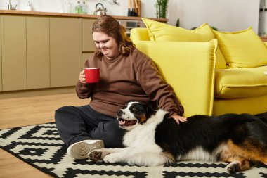 Genç bir kadın sıcak bir halıya oturmuş, evinde samimi köpeğiyle kahvenin tadını çıkarıyor..