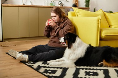 Down sendromlu genç bir kadın köpeğinin yanındaki kırmızı bardaktan yudumlarken yerde dinleniyor..