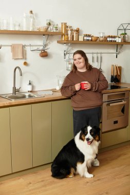 Down sendromlu genç bir kadın modern mutfağında elinde bir köpekle gülümsüyor..