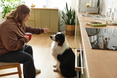Down sendromlu genç bir kadın evinde köpeğiyle oynarken sıcak bir içki içiyor..