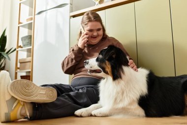 Down sendromlu genç bir kadın gülümseyerek ve konuşarak köpeğiyle iyi vakit geçiriyor..