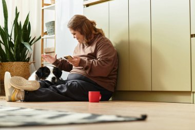 Down sendromlu genç bir kadın yerde oturuyor ve köpeği ve telefonuyla iletişim kuruyor..