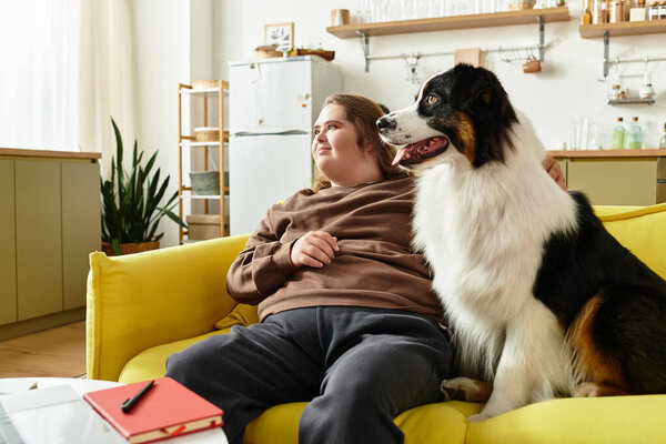A young woman with Down syndrome relaxes with her dog on a yellow couch at home.