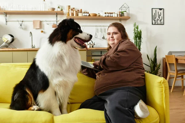 Genç bir kadın parlak bir kanepede oturuyor ve köpeğiyle oturma odasında mutlu bir şekilde vakit geçiriyor..