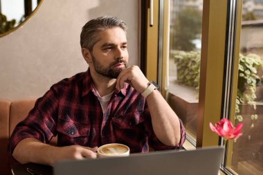 Moda gömlekli olgun bir beyefendi pencerenin yanında sıcak bir içecekle düşüncelerini yansıtır..