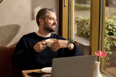 Şık giyinmiş olgun bir adam, sakin bir kafeye bakarken kahvenin tadını çıkarıyor..