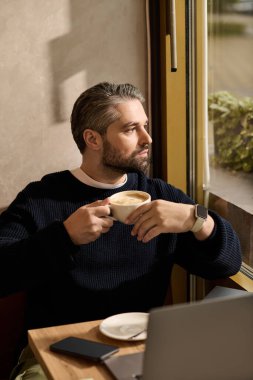 Şık giyinmiş yakışıklı adam kahveyi özenle yudumluyor, kafenin penceresinden dışarı bakıyor..