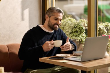 Şık, olgun bir adam kahve içer ve sıcak bir kafede dizüstü bilgisayarıyla çalışır..
