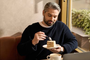 Tarz sahibi olgun bir adam, işine odaklanırken kafe masasında pasta yemekten hoşlanır..