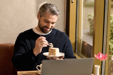 Yakışıklı, olgun bir adam kafeteryada otururken bir parça kek yerken gülümsüyor..