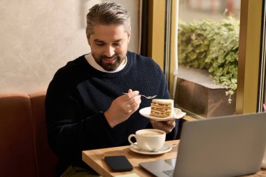Şık giyinmiş olgun bir adam, kafeteryada otururken kekin ve kahvenin tadını çıkarıyor..