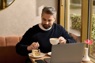 Yakışıklı adam sıcak bir kafe atmosferine dalmış kahvesini yudumlarken kekin tadını çıkarıyor..
