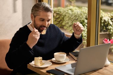 Yakışıklı, şık giyinen, kek ve kahveden zevk alan ve dizüstü bilgisayarıyla meşgul olan bir adam..