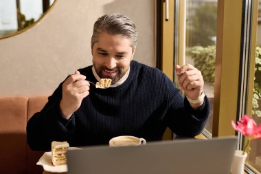 Şık giyinen yakışıklı adam, modern bir kafede otururken tatlının tadını çıkarıyor ve gülümsüyor..