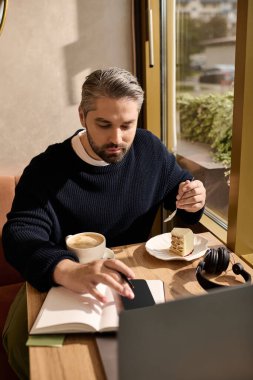Olgun bir adam, güneşli bir kafede kitap okurken kek ve kahvenin tadını çıkarır..
