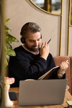 Şık kulaklıklı yakışıklı bir adam yeşilliklerle çevrili bir kafede yaratıcı işler yapıyor..