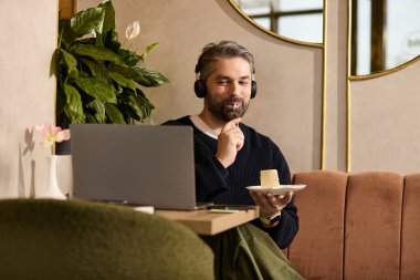 Olgun, yakışıklı bir adam, rahat bir kafede kulaklık takarken tatlı bir ziyafetin tadını çıkarır..