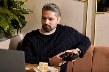 Olgun bir beyefendi şık bir kafede dinleniyor, kulaklıkla müzik dinlerken pastanın tadını çıkarıyor..