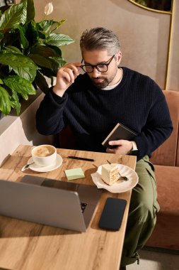 Yakışıklı, olgun bir adam ahşap bir masada oturur. Tatlının tadını çıkarırken kendini işine verir..