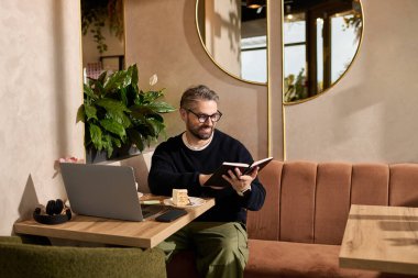 Yakışıklı bir adam bir kafede rahatlar, kitap okur ve bir dilim pastanın tadını çıkarır..