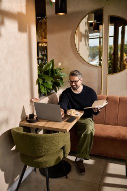 Rahat ve şık bir adam tatlının tadını çıkarırken dizüstü bilgisayarıyla ve menüsüyle meşgul olur..