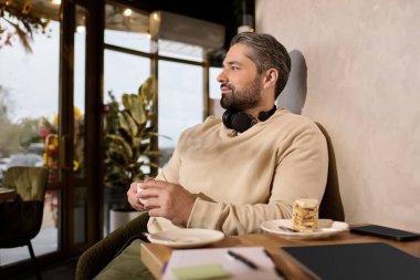 Tarz sahibi bir adam bir kafede rahatlar, tatlı bir ziyafetin tadını çıkarır ve havanın tadını çıkarır..