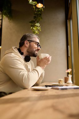 Tarz sahibi beyefendi sessizce ahşap bir masaya yansıyor, davetkar bir kafede bir fincan kahvenin tadını çıkarıyor..