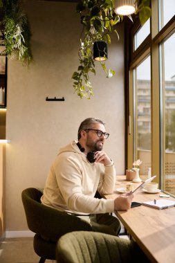Moda kıyafetleri içinde yakışıklı bir adam kafeteryada otururken düşünceli bir şekilde yazıyor..