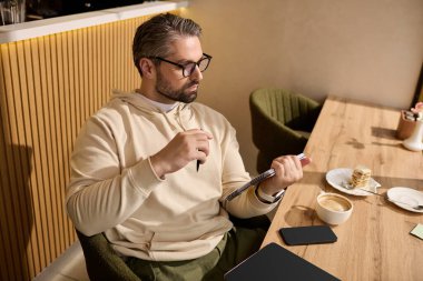 Moda kıyafetli yakışıklı adam bir kafede sıcak bir içecek içerken notlar yazmaya odaklanıyor..