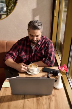 Şık giyinmiş yakışıklı bir adam kahvesinin tadını çıkarıyor ve sıcak bir kafe masasındaki görevlere odaklanıyor..