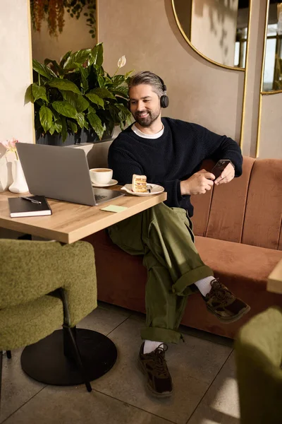 Yakışıklı, şık giyinmiş bir adam bir kafede dinleniyor, bilgisayarıyla ve kahveyle meşgul..