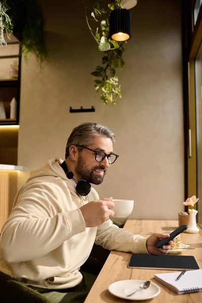 Hoş bir kafede yakışıklı, olgun bir adam telefonundaki mesajları kontrol ederken kahvesini yudumluyor..