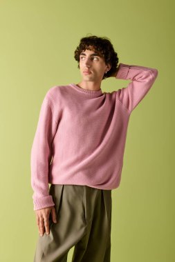 Pembe kazaklı ve rahat pantolonlu şık bir adam parlak yeşil bir fonda poz veriyor..