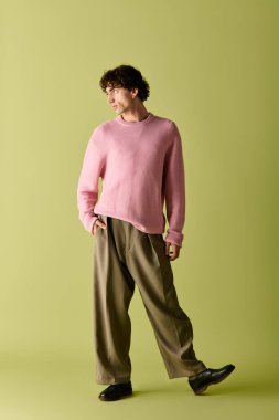 Pembe kazaklı ve bol pantolonlu iyi giyimli bir adam çekici bir ifadeyle rahatça poz verir..